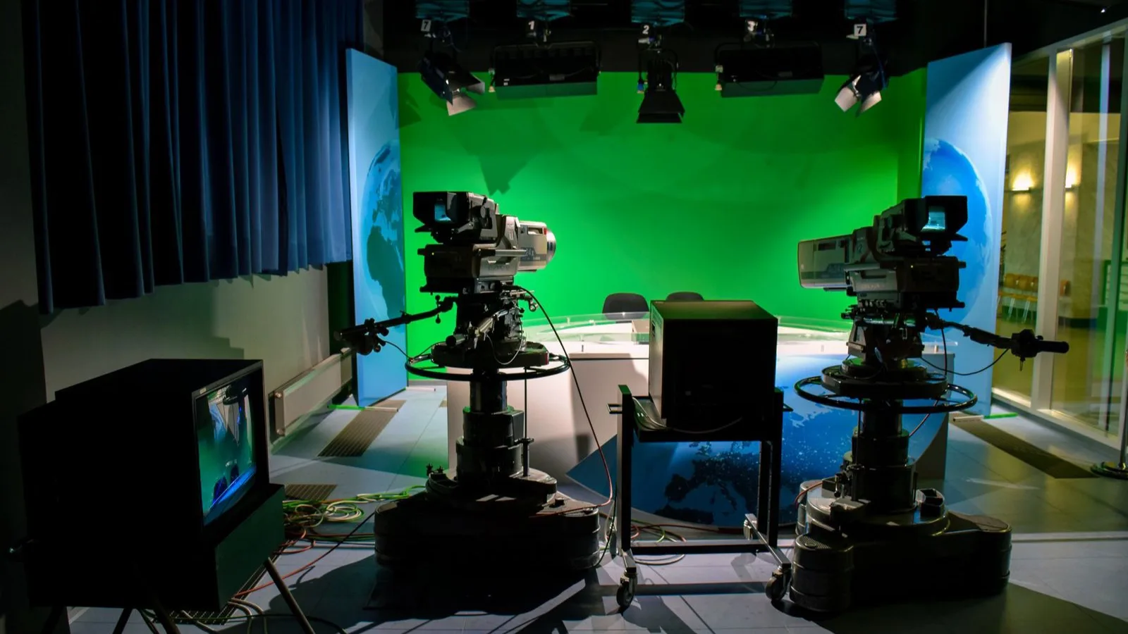A television studio with two broadcast cameras aimed at an empty green screen set.