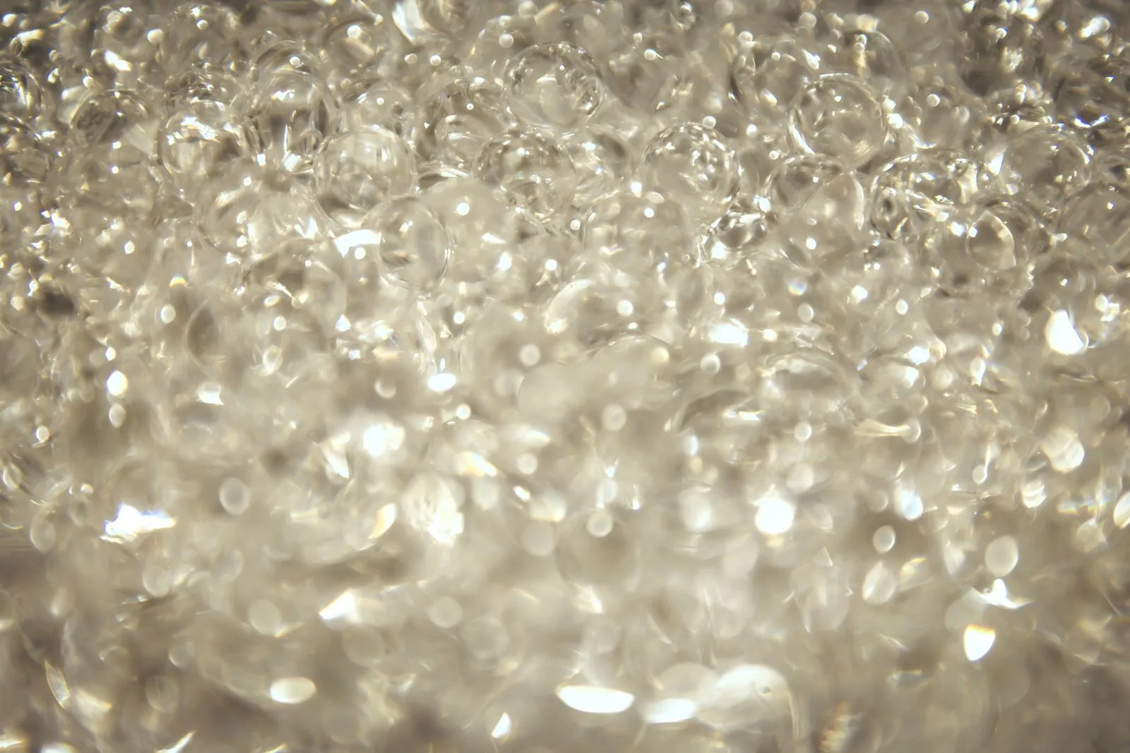 Extreme macro photograph of a dense heap of clear glass spheres packed edge to edge, each catching a bright specular highlight.