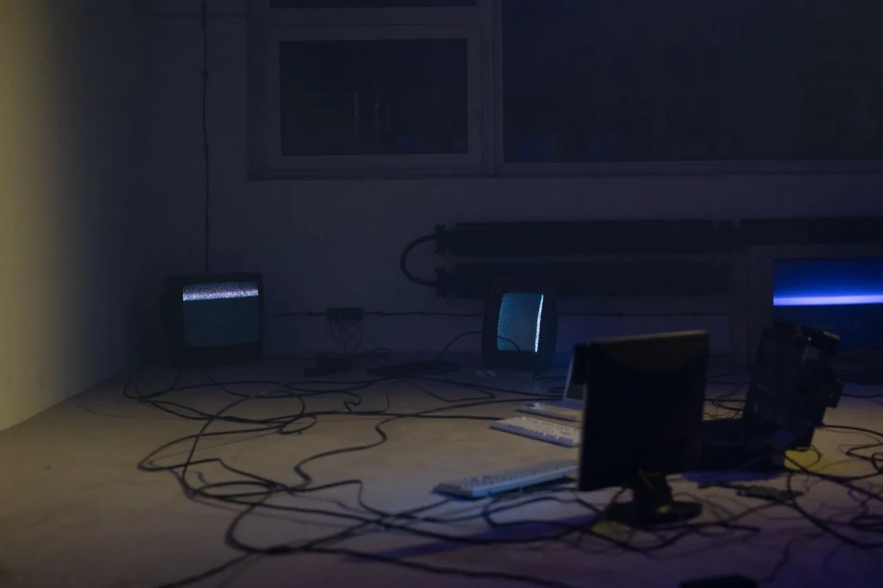 A dim room of old computers and CRTs trailing tangled cables across the floor.