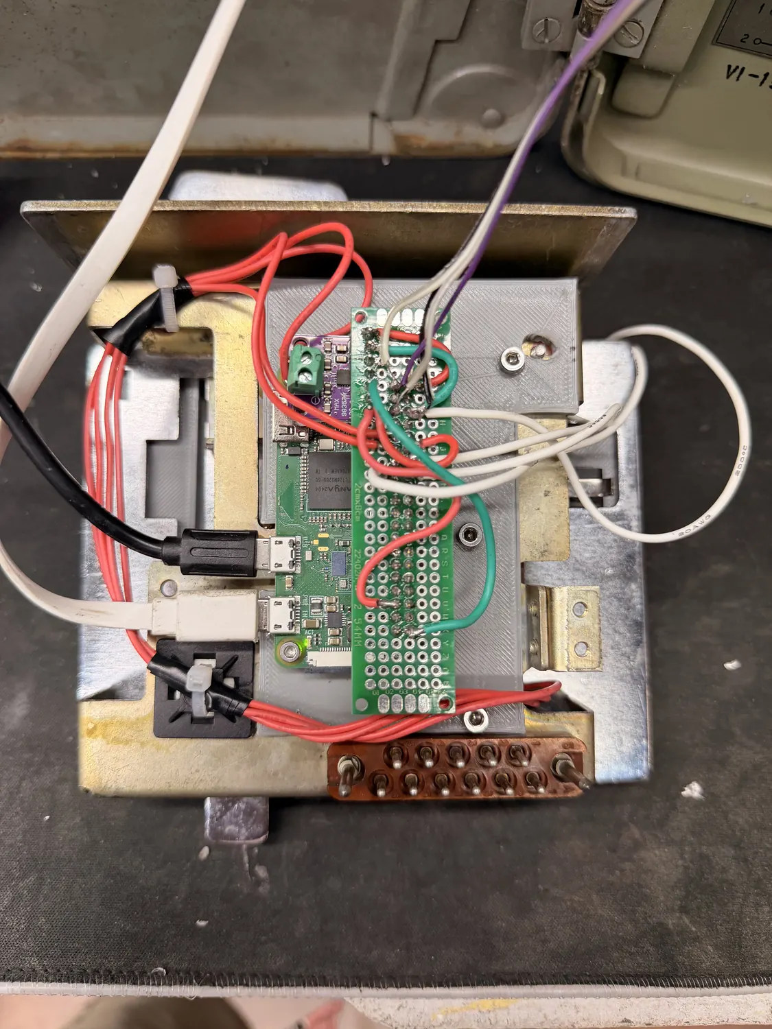 Top-down view of the printed mounting plate: a Raspberry Pi Zero and a MAX98357 amplifier board sit on grey printed standoffs, wired through a strip of green perfboard to a brass terminal strip along one edge, with red, white and green hookup wire running off the plate.