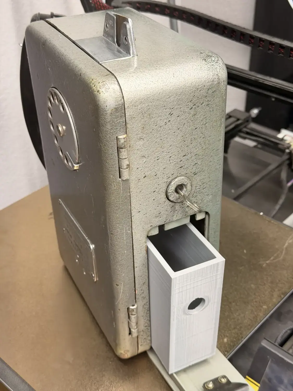 The payphone standing upright with a white 3D-printed coin bucket sliding out of its base.