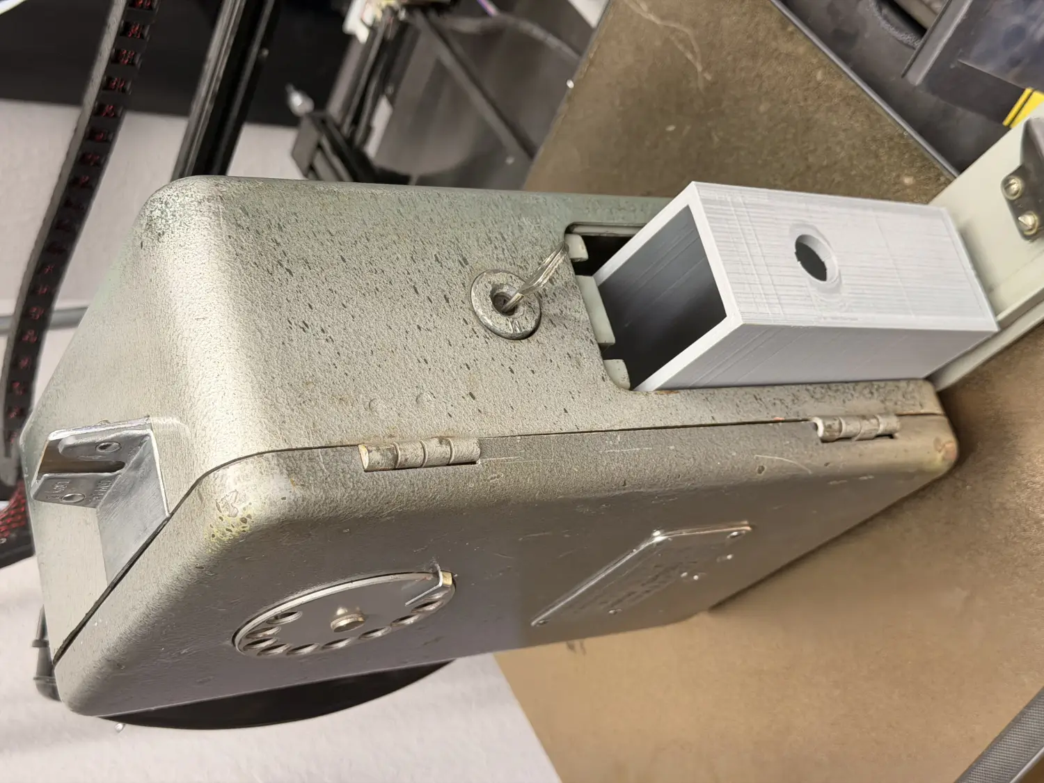 The payphone lying on its side with a white 3D-printed coin bucket sliding out of the base, next to the original cast-metal coin chute.