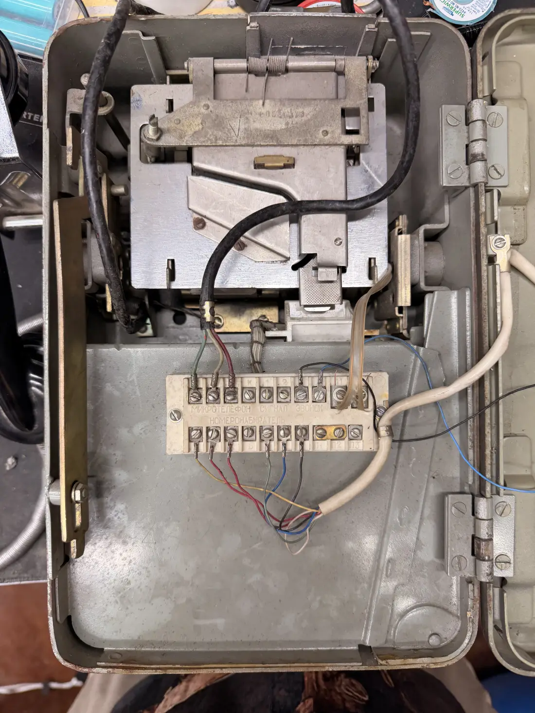 The open back of the payphone, showing the original coin mechanism bolted in on the left and a porcelain terminal block on the right, its terminals labelled in Cyrillic and wired with cloth-jacketed cable.